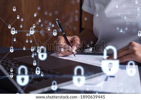 A businesswoman in casual wear signing the contract to prevent probability of risks in cyber security. Padlock Hologram icons over the working desk.