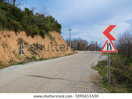 Traffic sign on mountain route with blue sky and green environment. Road narrows on right side.



