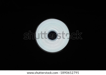 Bottom view of a circle-shaped lamp hanging from the ceiling, making an abstract picture of bright white circle surrounded by black shadow