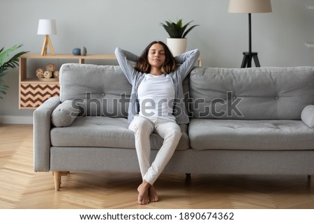 Full length peaceful woman with closed eyes resting on couch, leaning back with hands behind head, enjoying lazy weekend at home, calm young female relaxing, daydreaming, taking nap on sofa Royalty-Free Stock Photo #1890674362