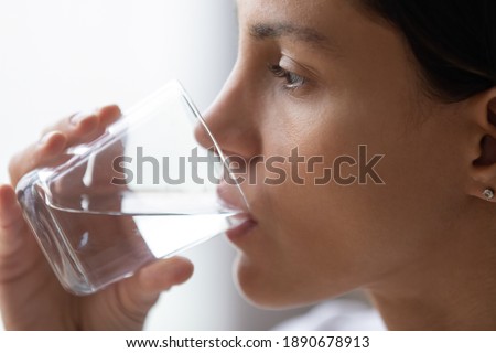 Close up cropped image beautiful thirsty woman with perfect skin drinking still pure mineral water, preventing dehydration, body balance, young female holding glass, healthy lifestyle habit concept