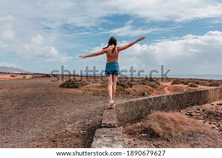 Young woman with arms outstretched balancing on a stone wall on a sunny day. Freedom, travel photography