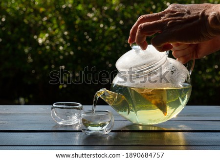 picture of people pouring hot water into clear glass kettle to make black tea in afternoon in garden