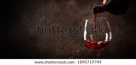 Pouring red wine into the glass against rustic dark wooden background Royalty-Free Stock Photo #1890719749