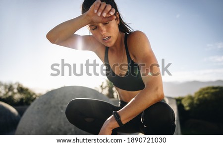 Tired woman sitting and resting after workout. Woman feeling exhausted after training session wiping her sweat from her forehead. Royalty-Free Stock Photo #1890721030