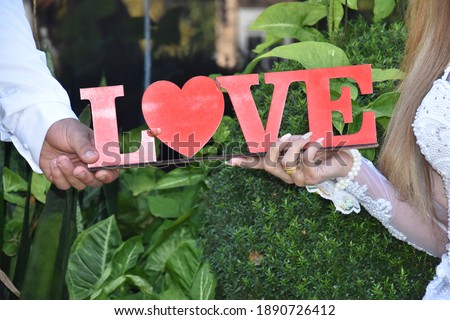 the hands of the bride and groom hold the word love made of red letters. High quality photo