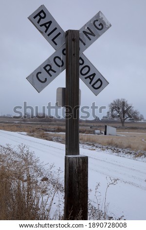 Old railroad crossing sign and barrels wooden post in the countryside.  Black and white old rail crossing sign with snowy background and rural setting.  