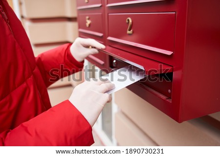 Cropped view of the young caucasian courier puts order in the mailbox in the entrance, while enjoying working in delivery company. Stock photo