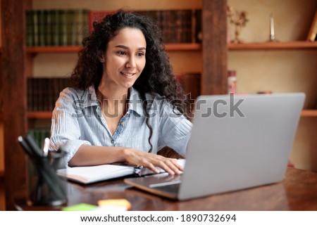 Doing Project. Portrait of curly young woman using laptop computer and typing on keyboard, writer sitting at table. Female manager working remotely or studying online at home, telecommuting Royalty-Free Stock Photo #1890732694