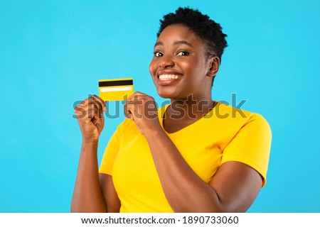 Oversized African Woman Holding Yellow Credit Card Showing It To Camera Advertising Bank Posing Over Blue Studio Background. Banking, Money And Finance, Financial Advertisement Concept Royalty-Free Stock Photo #1890733060