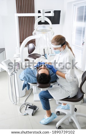 Professional woman dentist doctor working. Serious woman at dental clinic. Multiracial man at dentist taking care of teeth. Dental care for people. Dentist holding dental device for fixing teeth Royalty-Free Stock Photo #1890739102