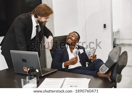 African man in a black suit. Guy sitting at the table. Businessman with money. International partners.