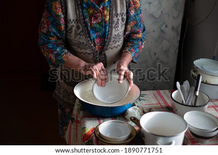 Russian grandmother washes dishes in a basin in the village