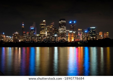 Colourful skyscraper lights reflecting in calm water at night.