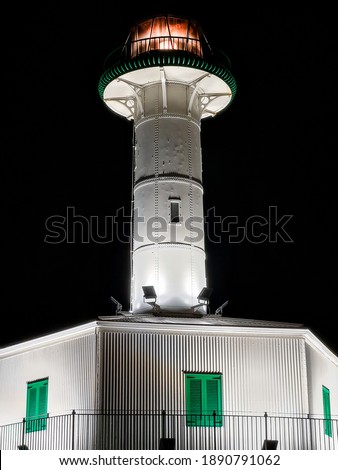Far de la banya, vintage lighthouse restored and placed at the harbor of Tarragona, it is currently a museum. White lighthouse tower with with green windows at night. Tarragona, Catalonia, Spain