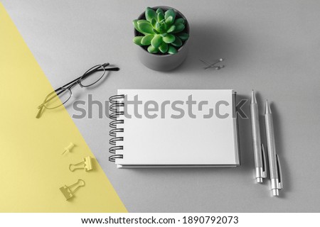 Open notebook, glasses, pens and succulent plant on grey desk. Image toned in illuminating and ultimate gray trendy colors 2021 year. Minimal workplace