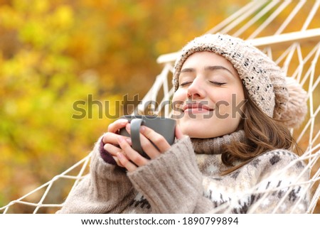 Relaxed woman smelling coffee lying on hammock in autumn holidays Royalty-Free Stock Photo #1890799894