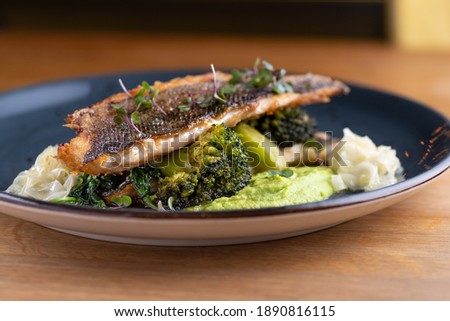 Grilled sea bass with broccoli and pea puree on the table, in a restaurant, menu food concept. Healthy balanced diet.