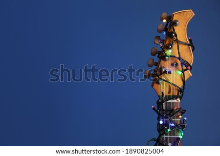 Guitar with festive lights on blue background, space for text. Christmas music