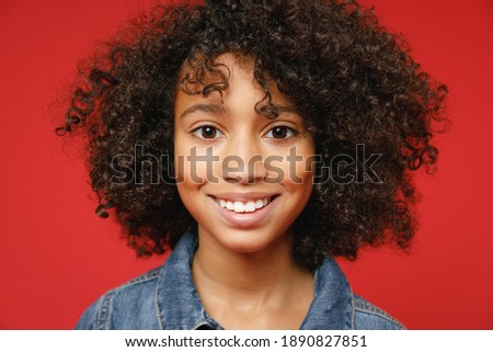 Close up of smiling little african american kid girl 12-13 years old wearing casual denim jacket looking camera isolated on red color background children studio portrait. Childhood lifestyle concept