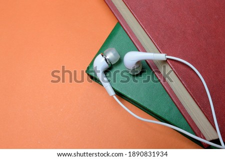 small white, wired headphones lie on top of a stack of books. close-up