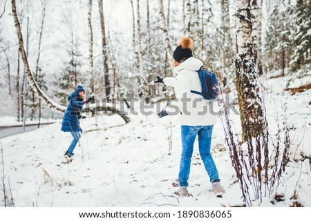 Two women throw snowballs in the forest - white trees in winter