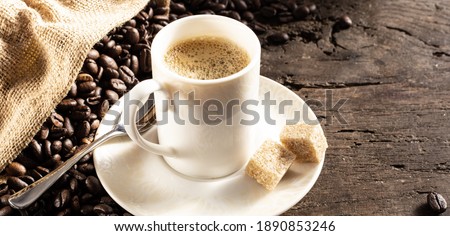 Rustic background with cup of coffee espresso in white porcelain cup with roasted coffee beans on old wood background with canvas bag. Morning cup of coffee concept