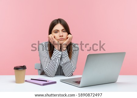 Bored inefficient woman office employee sitting at workplace leaning head on hands, lonely disappointed female tired of wimp work. Indoor studio shot isolated on pink background