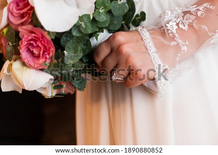 Close up picture of bride's hand, diamond engagement ring on finger,white lace long sleeve dress, holding round elegant wedding bouquet of the roses, orchids and greens