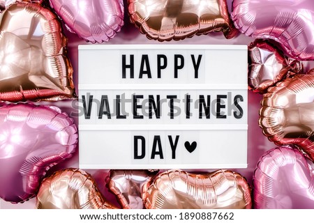 Stylish text frame lightbox with the inscription happy Valentine's day. Pink and beige hearts all around. Foil balloons top view of Valentine's Day. Copyspace.