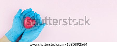 Doctor hands with blue medical gloves holding red heart, medical insurance concept. Symbol of the heart in the hands of a doctor on pink background