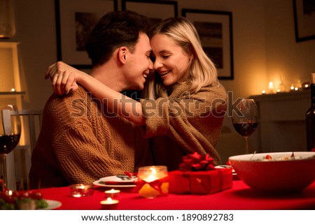 Happy affectionate young couple in love hugging laughing, drinking wine, celebrating Valentines day dining together, having romantic dinner date in candle light sit at home table on Valentine's day. Royalty-Free Stock Photo #1890892783