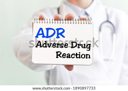 Doctor holding a card with text ADR - short for Adverse Drug Reaction, medical concept. The text is written in blue fnd blsck letters in a medical journal.