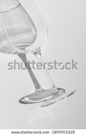 A part of wine glass lies on white background. Glass with hard shadow on  white table. Black and white photo. Monochrome stock photo.