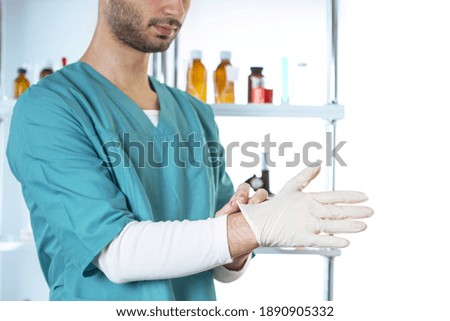 Cropped view young doctor in medical apparel puts on latex glove. Lifestyle outdoor scene