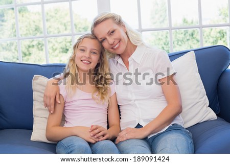 Portrait of happy mother and daughter sitting on sofa at home
