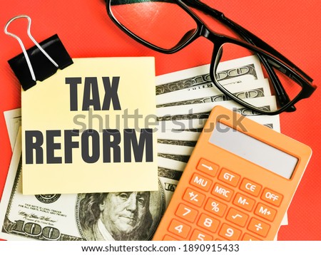 Text TAX REFORM written on paper notes with calculator,fake money and eye glasses isolated on red background.Business and finance concept.