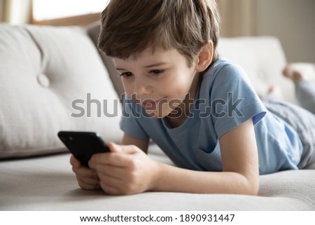 Close up of cute little 7s Caucasian boy child look at cellphone screen play online game on gadget. Happy small preschooler kid have fun using smartphone device with wireless internet connection.