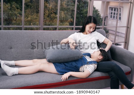 Smiling Asian mother and little girl child is relaxing and laying together on sofa in living room. Family time for mom and daughter Concept