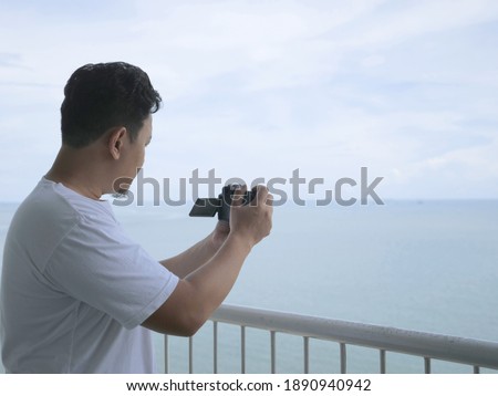 Man taking pictures of the ocean with his camera from his balcony, traveling tourism concept