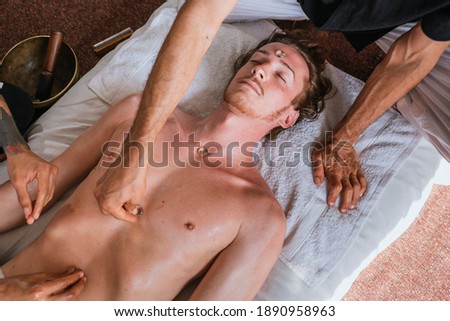Stock photo of relaxed man lying in the floor and receiving body massage with natural plants.
