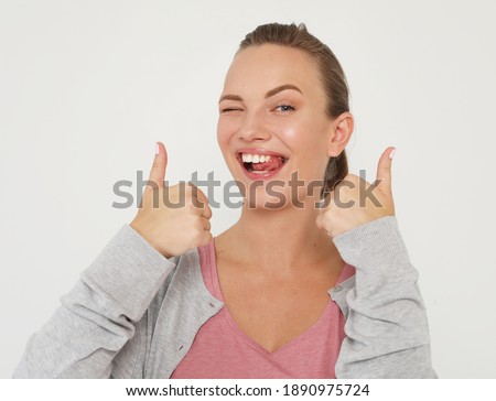 lifestyle, emotion and people concept: Portrait of a happy young blond female showing ok gesture and winking, studio shoot.