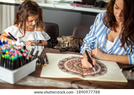 Mom and daughter are doing Zen painting together in their home in the kitchen. Concept for meditation, doodle drawing and hobbies.