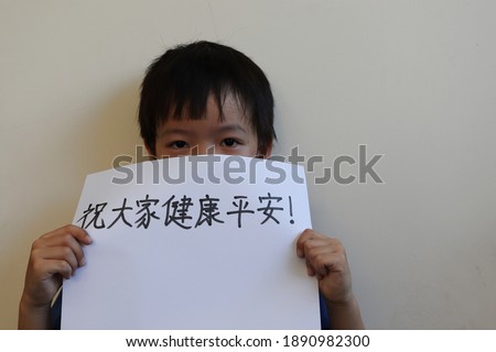 Asian boy holding white paper with text in Chinese means "Stay safe and healthy" as for policy campaign to control COVID-19 during Coronavirus outbreak situation.