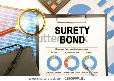 Business and finance concept. On the table are charts with reports, a notebook, a magnifying glass and a document with the inscription - SURETY BOND Royalty-Free Stock Photo #1890999181
