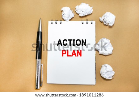 On a yellow background next to a pen and crumpled sheets of paper is a notebook on which the word action plan is written. The concept of planning