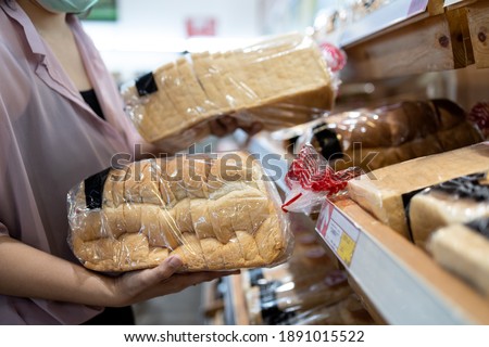 Hands of girl holding sliced white bread product,choosing wheat bread in plastic bag packaged,fresh homemade baked bread in the bakery shop while shopping food,woman buying or selecting food quality Royalty-Free Stock Photo #1891015522