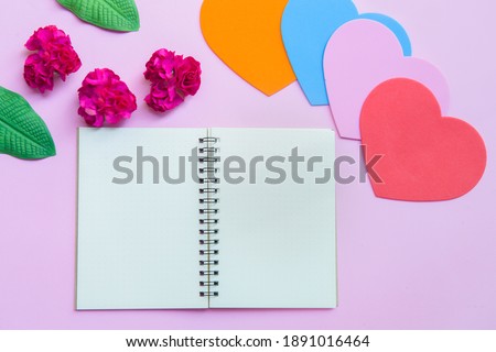 Notebook paper  and  paper hearts on pink paper background. Romance and St. Valentine's Day concept. Top view, copy space for text.