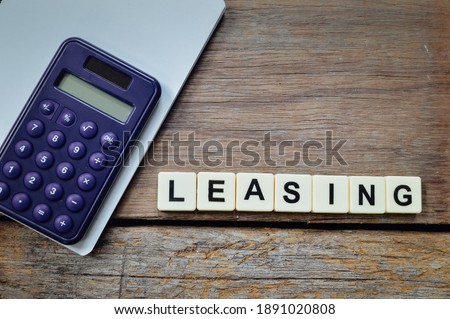 Top view of calculator, notebook and alphabet letters with text LEASING over wooden background. 