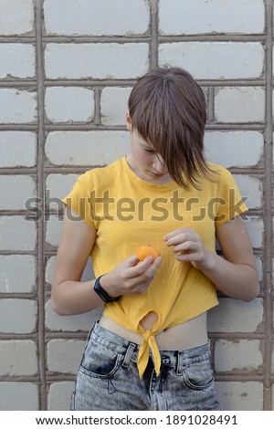 A Zen generation girl holds a yellow tomato grown at home. Brick wall background. The concept of gardening and agriculture. Greenhouse products and local shop